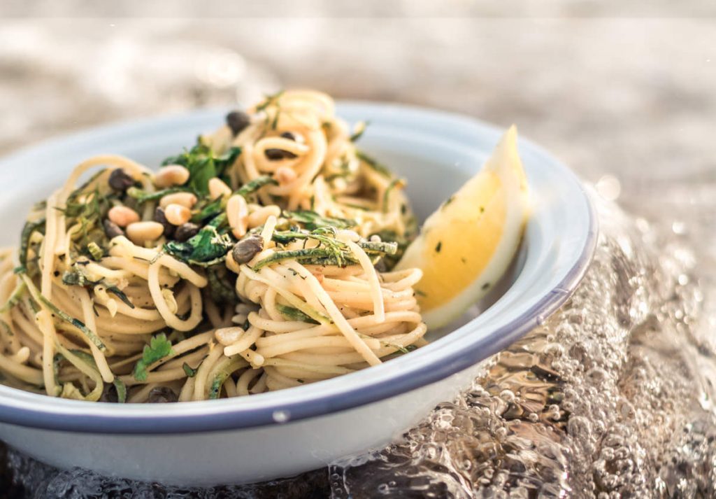 Gourmet Lemon, capers and dill spaghetti pasta bowl with pine nuts. Ocean waves splash over the dish for fresh concept.